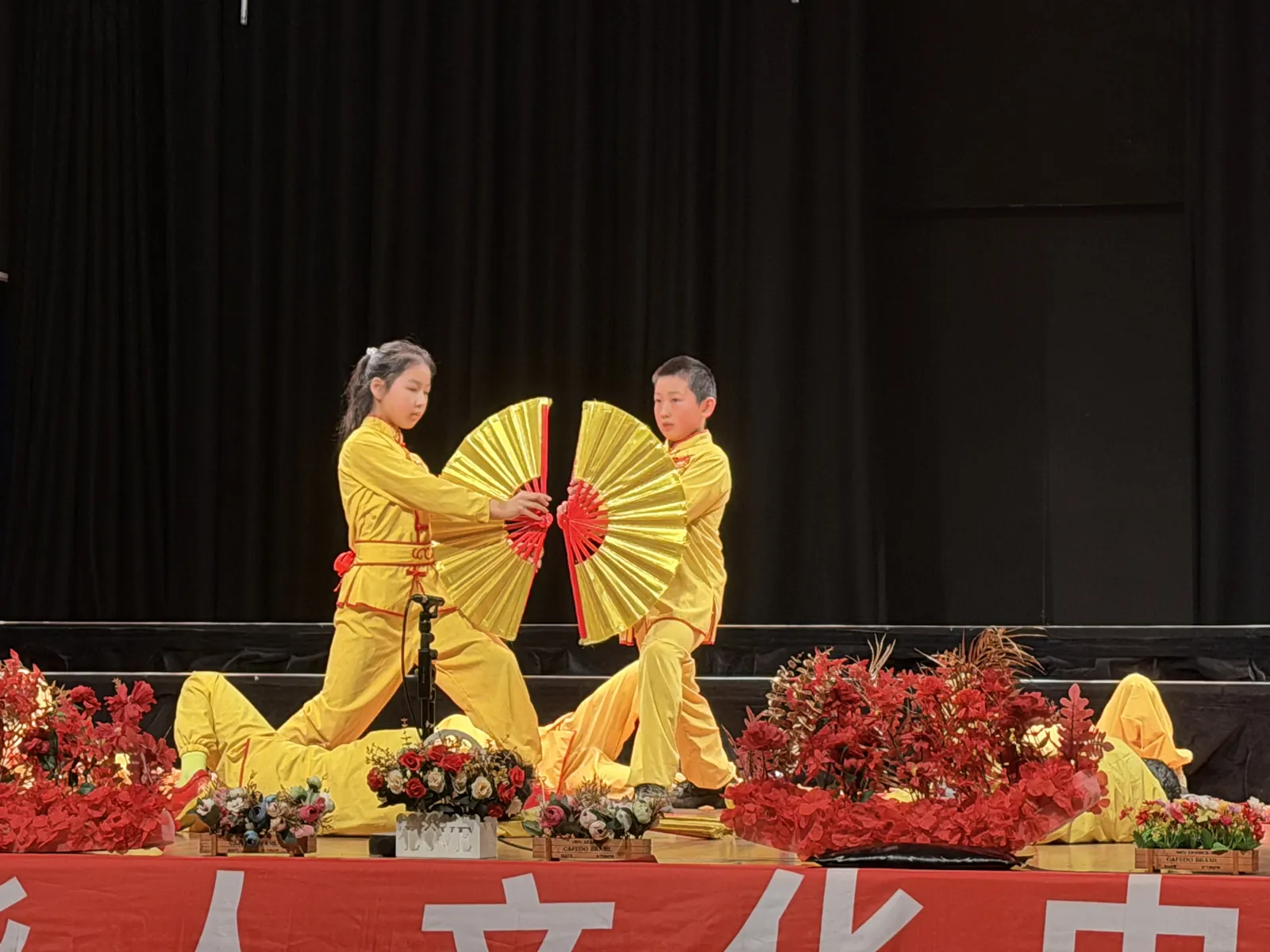 墨爾本舞臺上，身穿黃色功夫服的一男一女兩名孩子手持金色大功夫扇表演