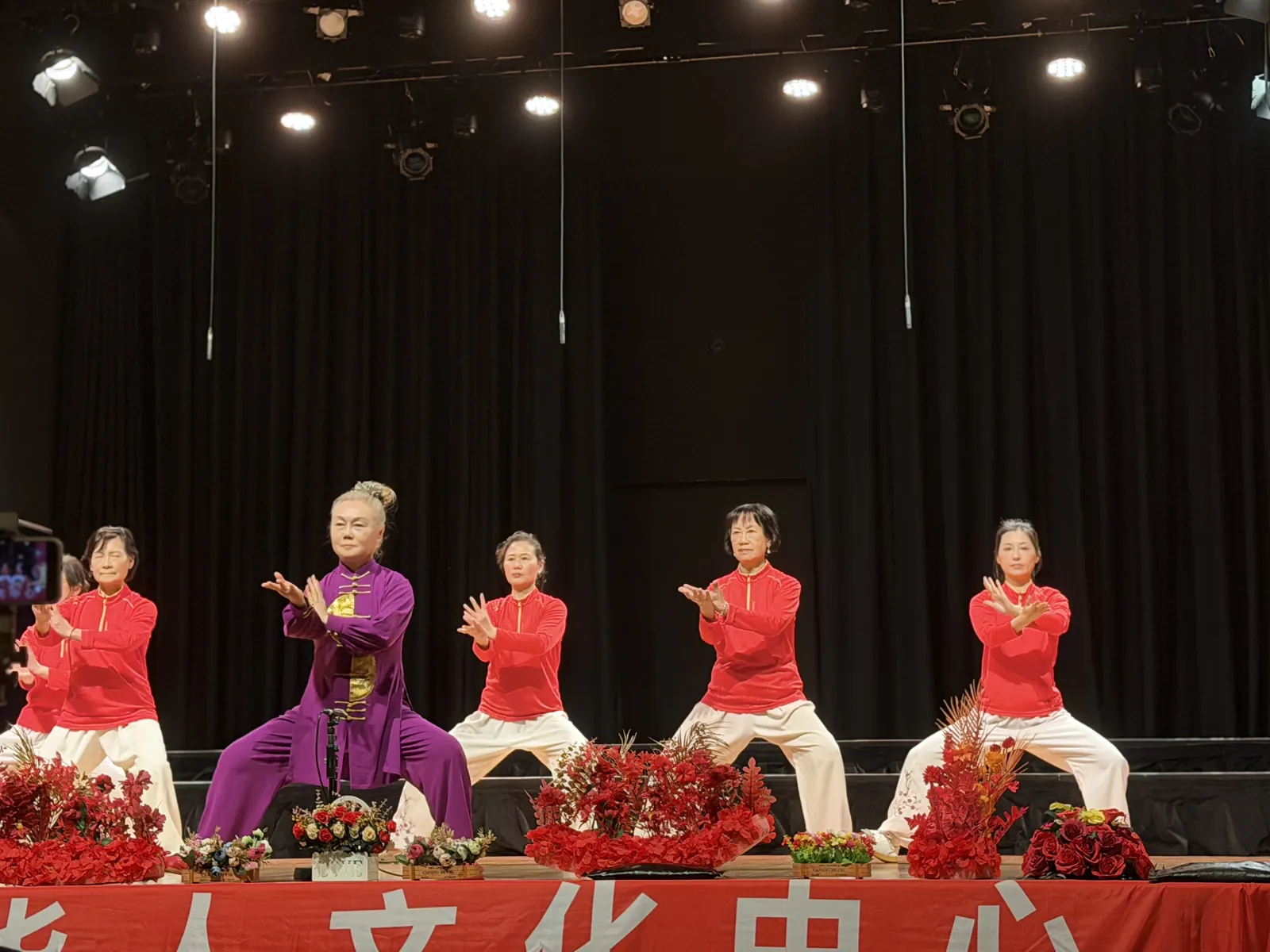 Senior Tai Chi practitioners in red and purple uniforms performing Chen-style Tai Chi on stage at Hawthorn Arts Centre, Melbourne
